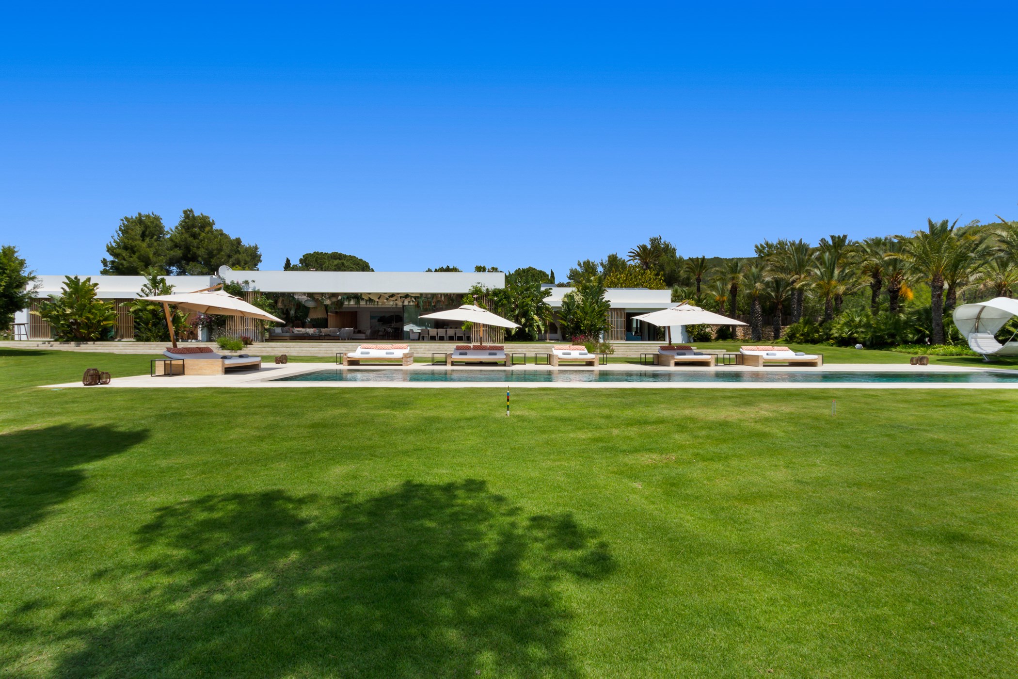 Wide view of the modern white villa, flat green lawn, and large pool