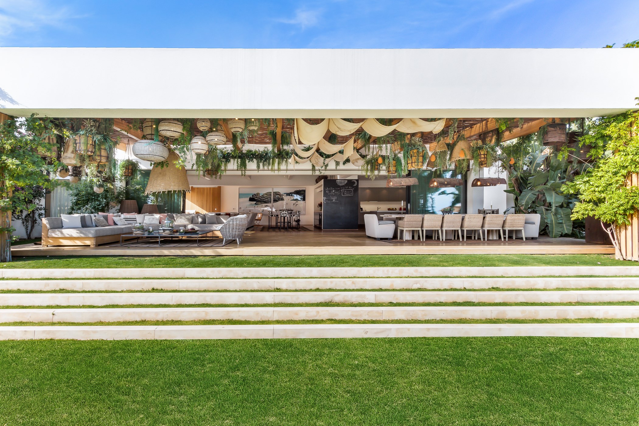 Covered outdoor terrace with a long dining table, seating area, and hanging plants