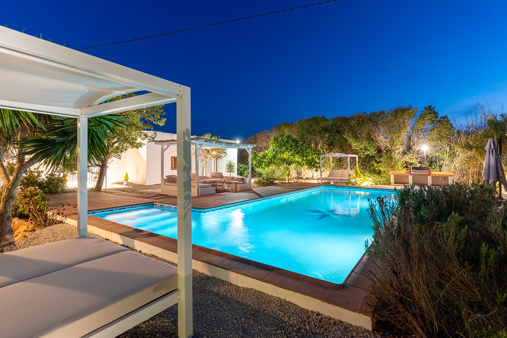 White sunbed cabana beside the swimming pool and an outdoor barbecue area at dusk.