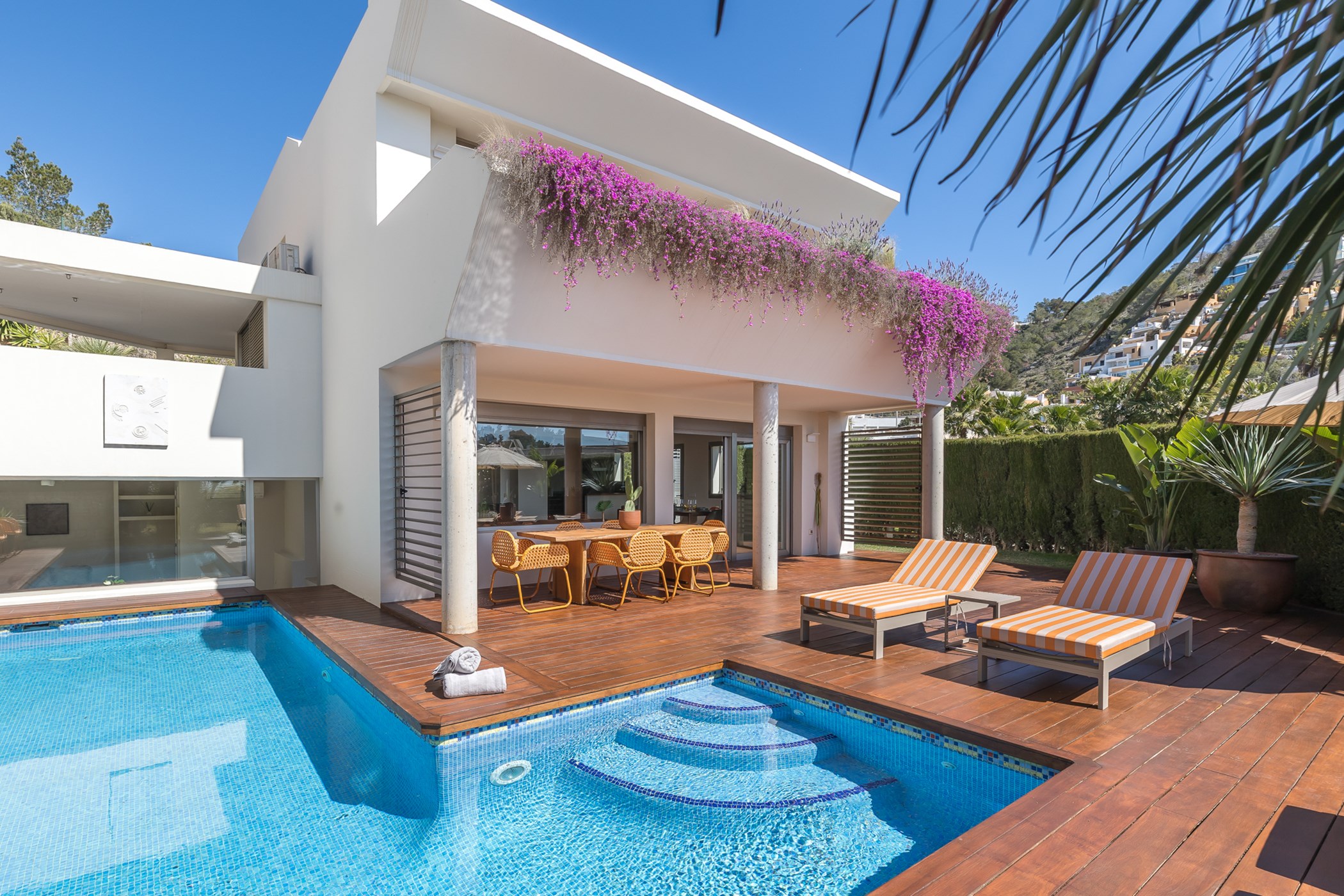 Swimming pool with built-in steps, surrounded by wooden decking and covered dining terrace