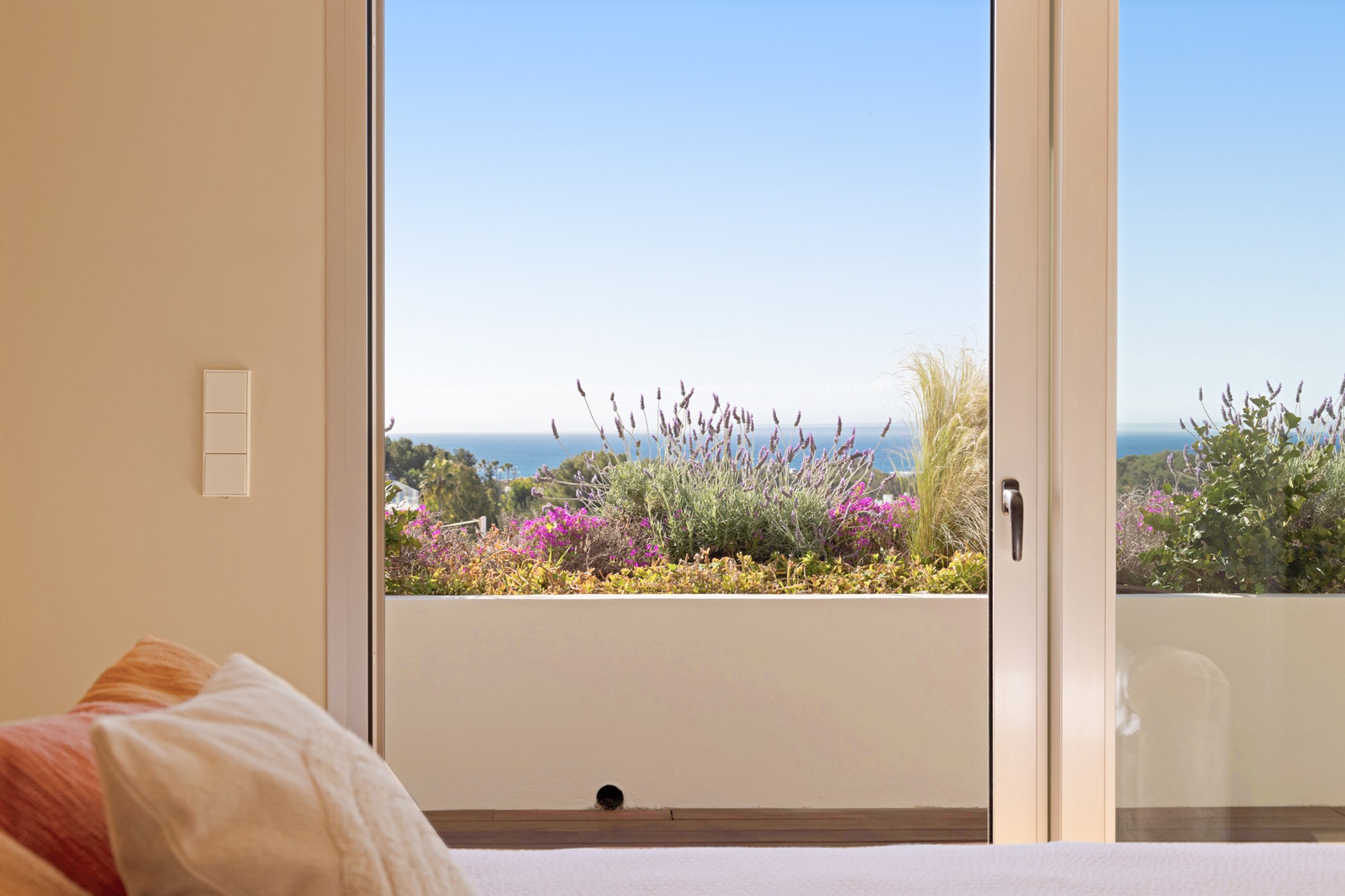 View from a bed looking past a planted terrace towards the blue sea