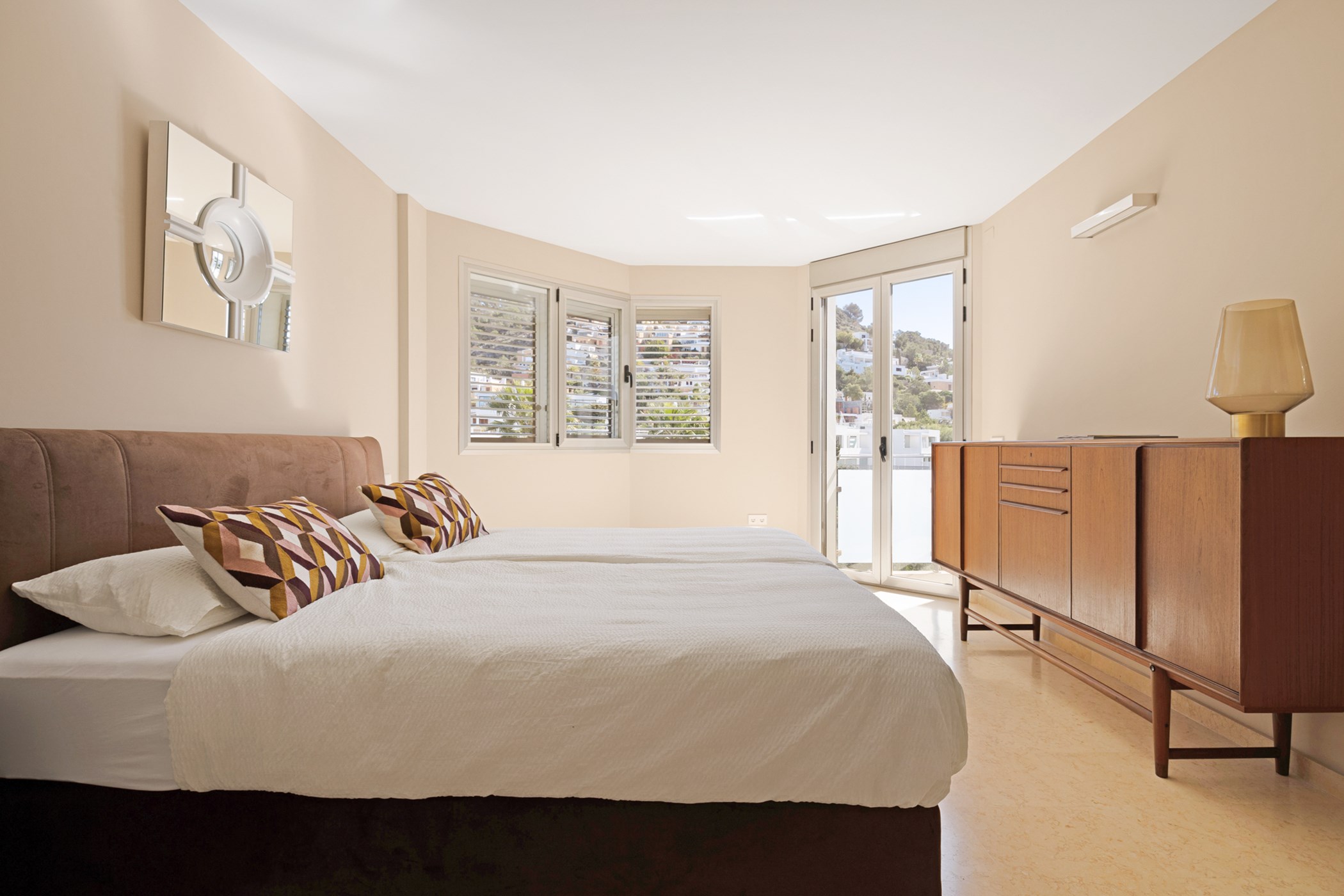Double bed with patterned cushions, a vintage wooden sideboard, and glass balcony doors