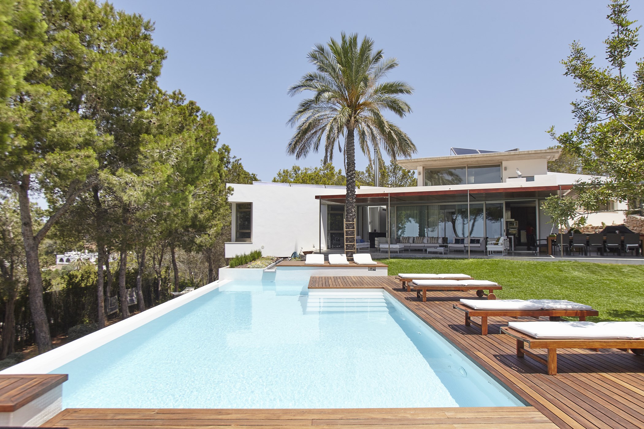 Modern white villa exterior, swimming pool, wooden decking, lawn, and covered dining terrace.