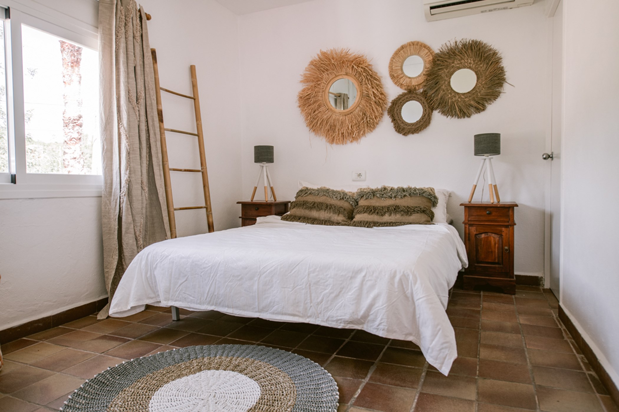 Bedroom featuring terracotta floor tiles, a double bed, and woven wall mirror decorations
